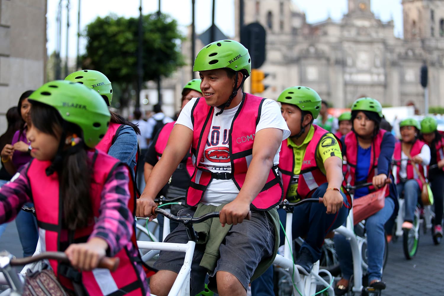 A long line of riders in matching vests and green helmets rolling down a city street